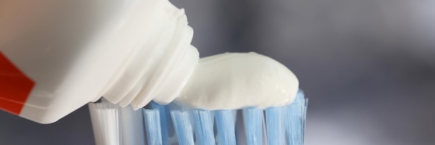 Squeezing white toothpaste onto toothbrush tube of tooth paste and tooth brush with blue