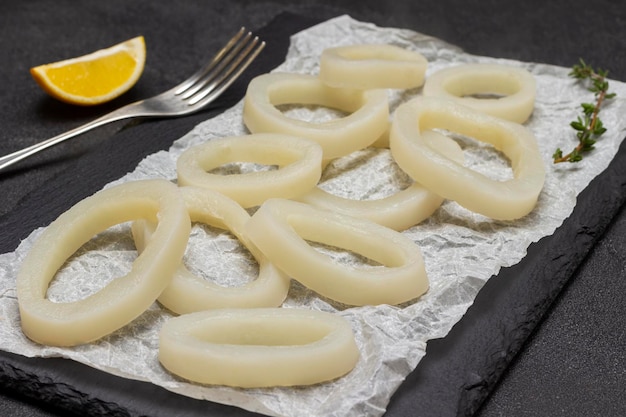 Foto calamari tagliati ad anelli su tavola di pietra forchetta e limone sul tavolo vista dall'alto sfondo nero