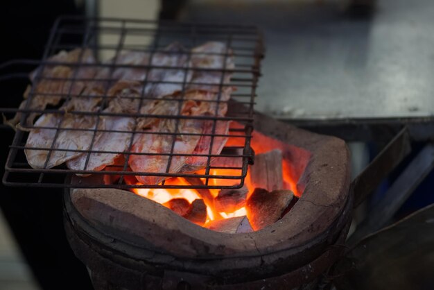 金属ふるいのイカグループが炭火ストーブ屋台の食べ物市場タイで焼いている