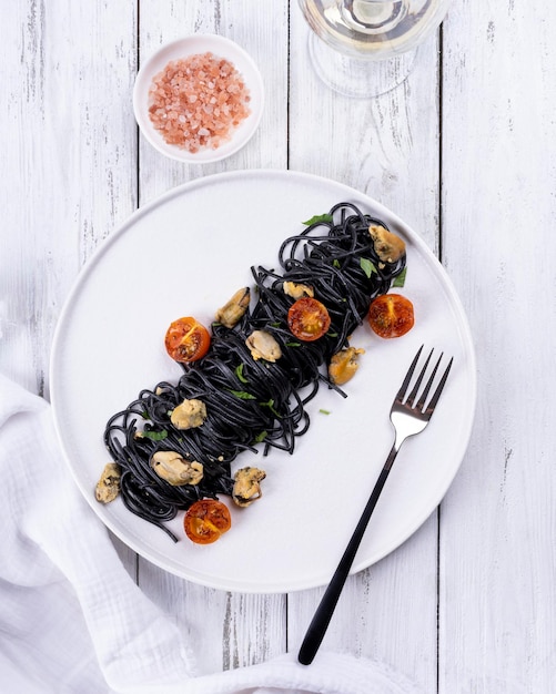 Squid ink pasta with seafood: mussels on a white plate on a white wooden background