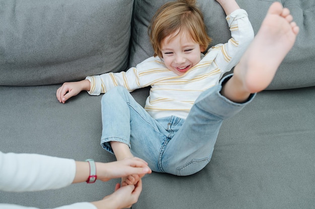 Squirming laughing boy being foottickled on the couch by girls hands