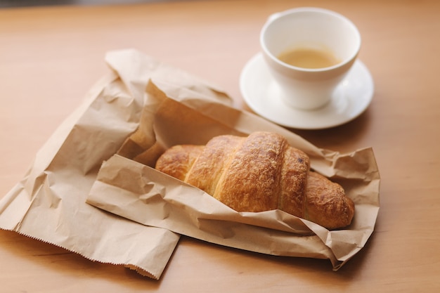 Sroissant en kopje koffie op houten tafel. Ochtend thuis.