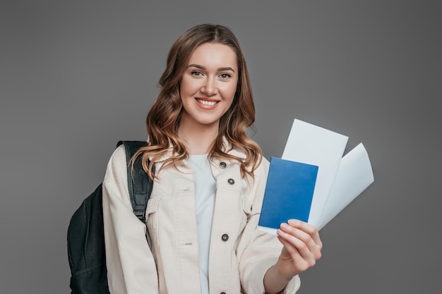 Concetto di studio all'estero. ragazza studentessa con zaino, libro, notebook, passaporto isolato su uno sfondo grigio scuro, copia spazio, immigrazione,