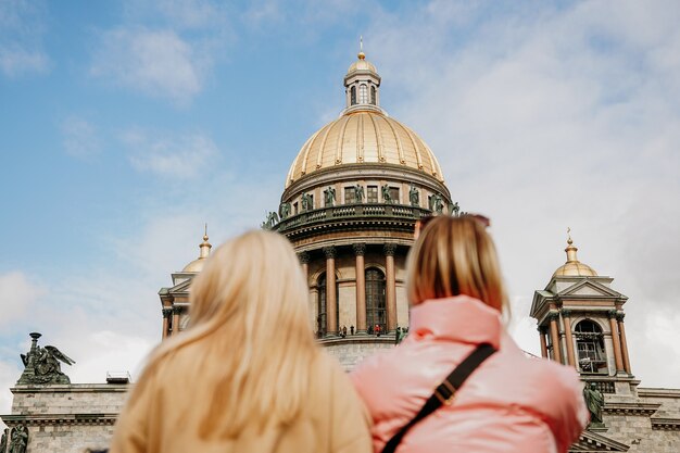 Photo st. isaac's cathedral in st. petersburg. blurred foreground - two tourist girls. focus on the cathedral. sightseeing and excursion concept