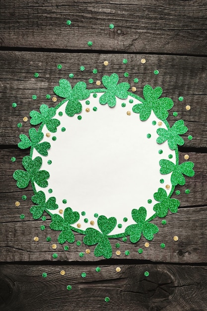 Foto st. patrick's day achtergrond rond frame van glanzende shamrocks en confetti op ruwe houten achtergrond