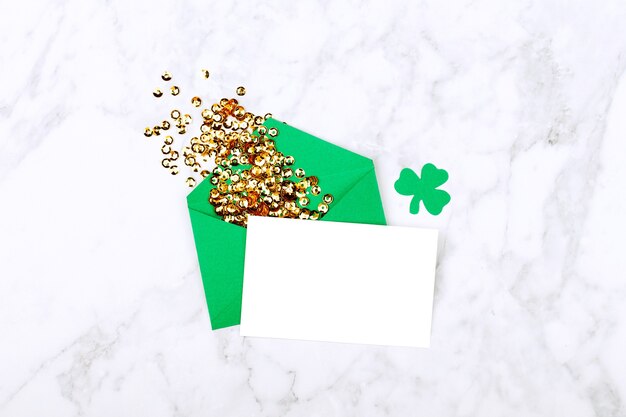 Photo st. patrick's day concept. empty card with green envelope and gold confett and clover leafi. mockup template. view from above