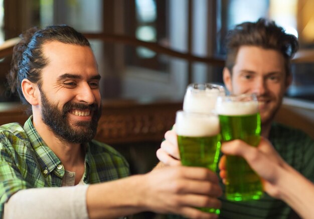 Foto st. patrick's day en feestconcept gelukkige mannelijke vrienden die groen bier drinken en glazen klinken in een bar of pub