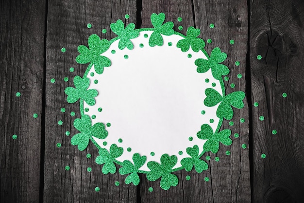 Photo st. patricks day background. round frame of shiny shamrocks and confetti on rough wooden background.