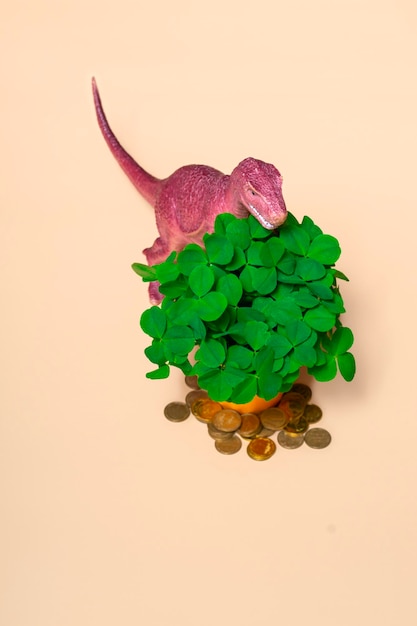 Photo st patricks day happy dinosaur a bouquet of clover in a bucket and gold coins on a beige background vertical format close up copy space