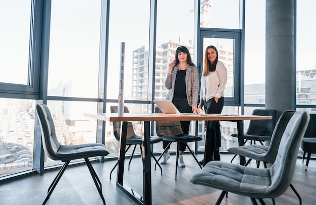 Staan en praten Twee vrouwen in formele kleding is binnen in het moderne kantoor werkt samen