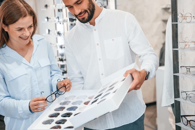 Staand en glimlachend Man en vrouw in de brillenwinkel Helpen bij het kiezen van een product