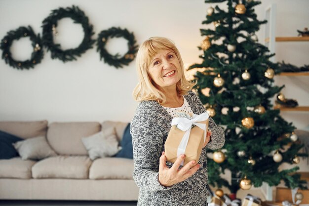 Staande bij de kerstboom Senior vrouw met blond haar is thuis