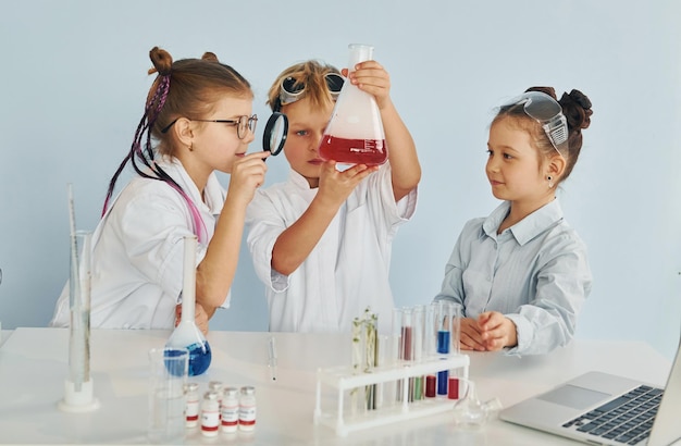 Staande bij de tafel met reageerbuisjes Kinderen in witte jassen spelen een wetenschapper in het lab met behulp van apparatuur