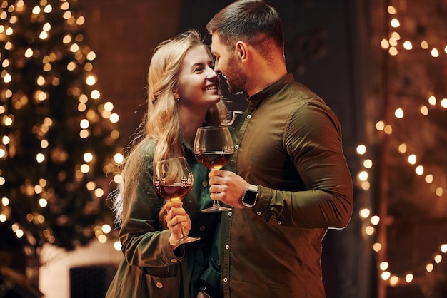 Staande en grote glazen met wijn vasthoudend jong mooi stel heeft samen romantisch diner binnenshuis