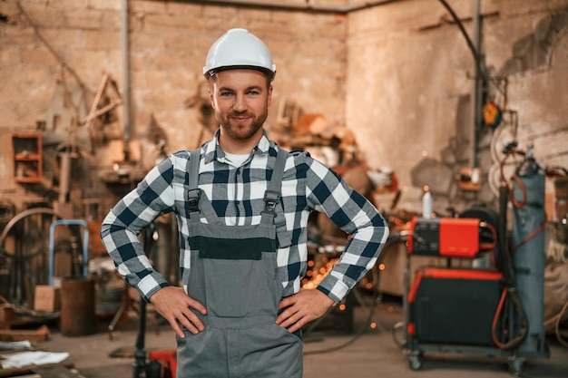 Foto staande handen zijn op de taille mannelijke fabrieksarbeider in uniform is binnen