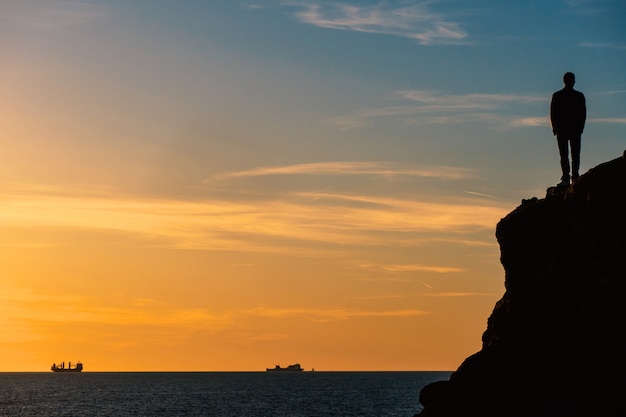 Foto staande man silouette op een rots voor de zee bij zonsondergang