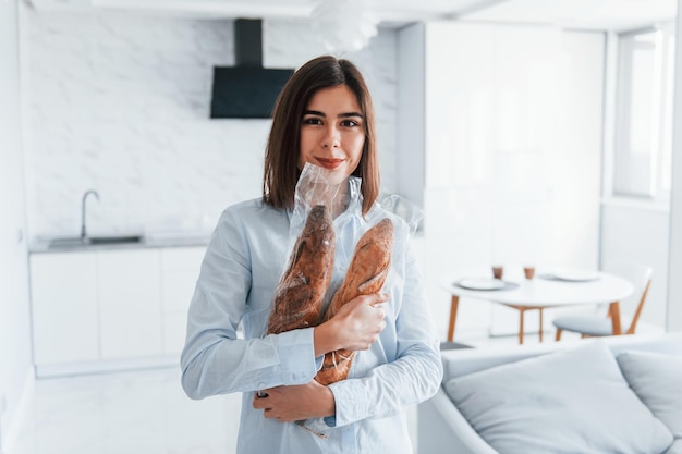 Staande met stokbroden jonge vrouw is overdag binnenshuis in de kamer van een modern huis