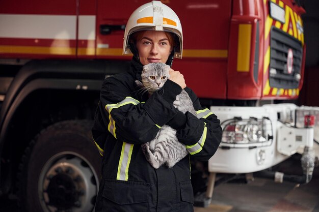 Staande tegen grote vrachtwagen en mooie kat vasthouden vrouw brandweerman in uniform is aan het werk