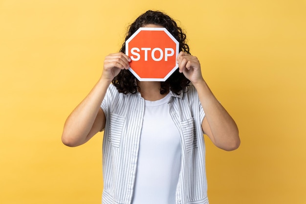 Foto staande vrouw die haar gezicht bedekt met een rood stopbord dat waarschuwt voor problemenconcept ban