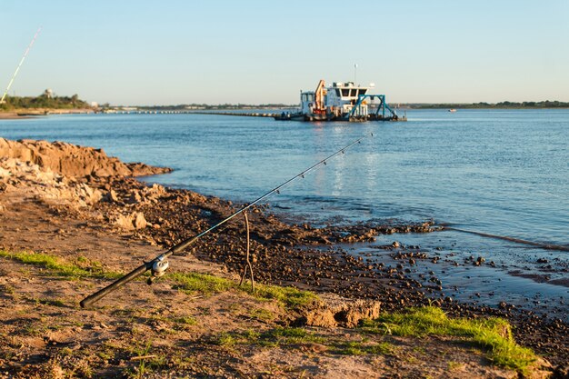 Stable fishing rod with a wooden pole on the shore of the river.