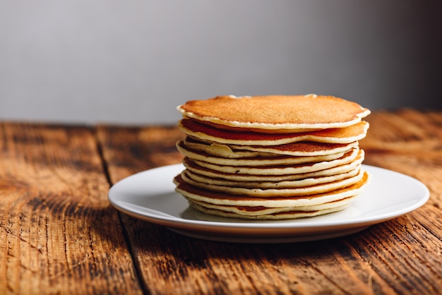 Stack of american pancakes on white plate over wooden table