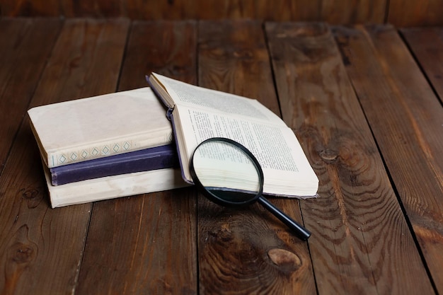 Stack of antique books with magnifying glass on wooden table