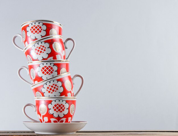 Stack of antique ceramic cups on a wooden table against a white wall