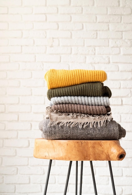 Stack of autumn warm sweaters on modern coffee table white brick wall background