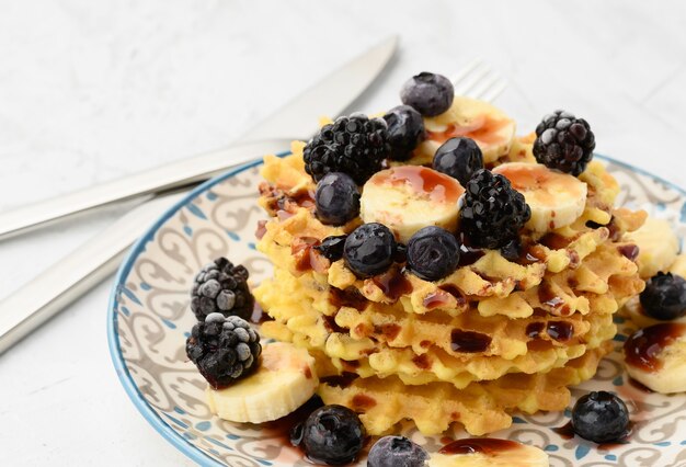 Stack of baked Belgian waffles on a round plate with berries on a white table, delicious breakfast