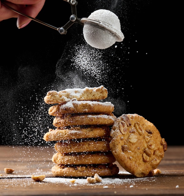 A stack of baked round cookies sprinkled with powdered sugar on a wooden table, black background