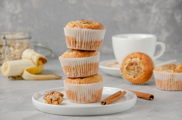 Stack of Banana muffins with oatmeal, walnuts and cinnamon on a white plate with a banana and a cup