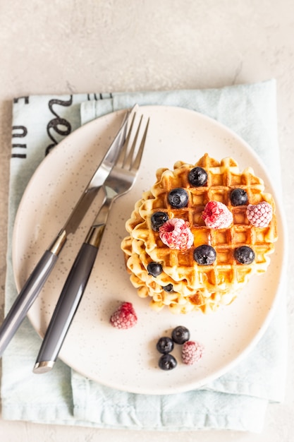 Stack of belgian vanilla waffles with berry (blueberry and raspberry) and honey.