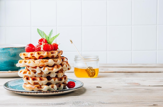 Stack of belgian waffles with honey mint and fresh raspberries on turqouise plate