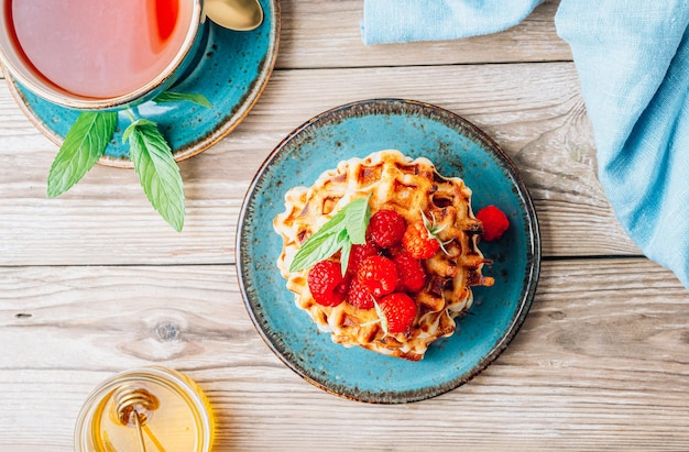 Stack of belgian waffles with honey mint and fresh raspberries on turqouise plate