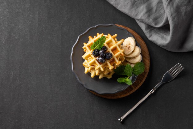 A stack of belgian waffles with kiwi banana slices and mint drizzled with honey syrup on a gray plate on a dark background