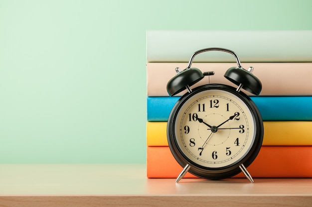 Stack of books and alarm clock on wooden table