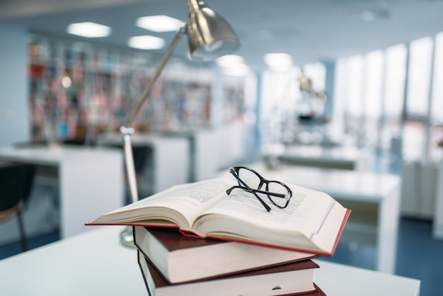 Stack of books and glasses on the table in university library, nobody. Knowledge depository, education concept