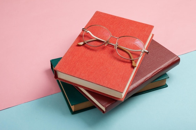 Stack of books and optical eye glasses on blue pink pastel background