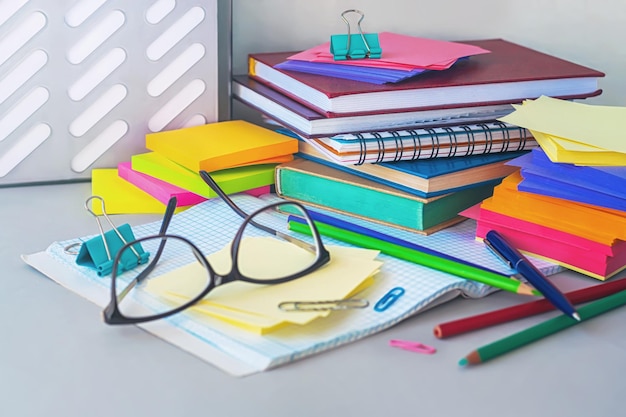 A stack of books a pair of glasses a pen and color pencils on the desk