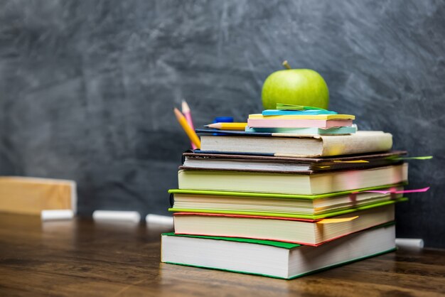 Stack of books, stationery and education supplies on the table in classroom