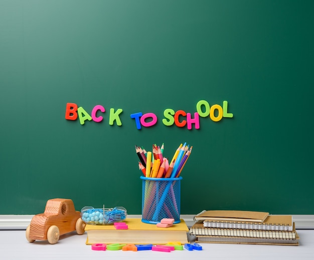 Stack of books and stationery on empty chalk green chalkboard background, back to school