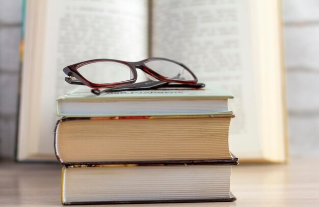 A stack of books with glasses and an open book in the background