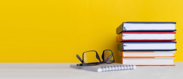 Photo stack of books with glasses on wooden desk on colorful yellow wall background