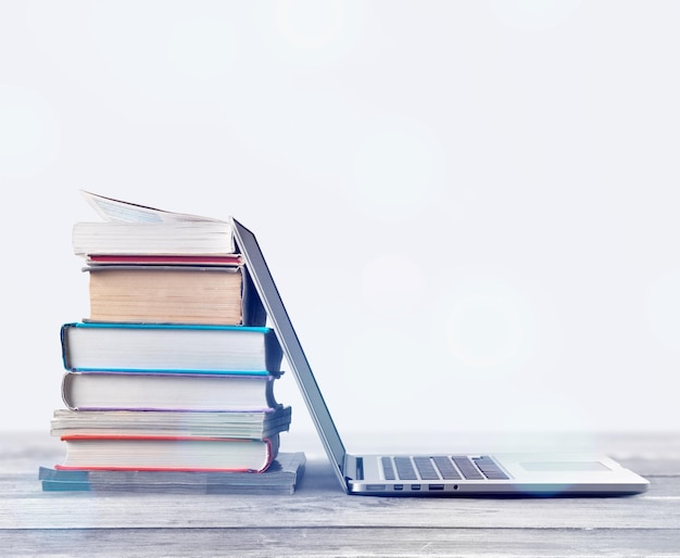 Stack of books with laptop on wooden table