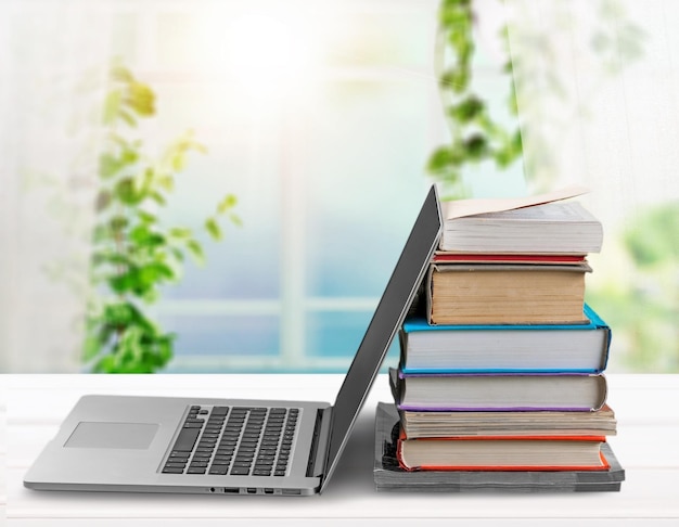 Stack of books with modern laptop on table