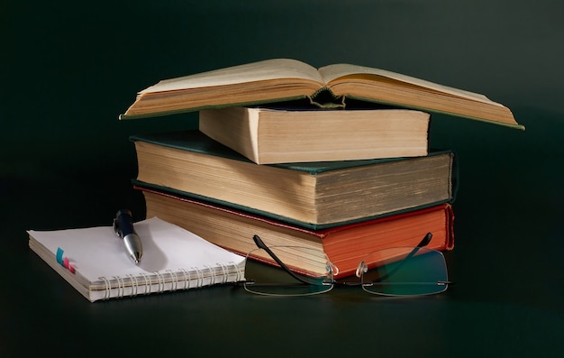 A stack of books with a notebook and a pen