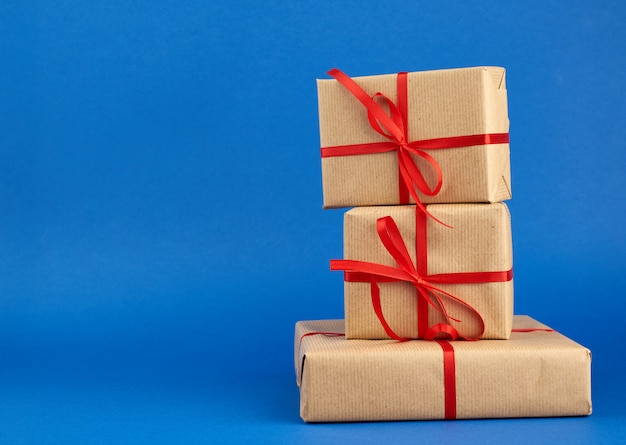 Stack of boxes wrapped in brown paper and tied with a red bow, gifts on a blue background