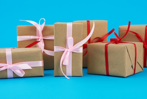 Stack of boxes wrapped in brown paper and tied with a red bow, gifts on a blue . Great design for any purposes