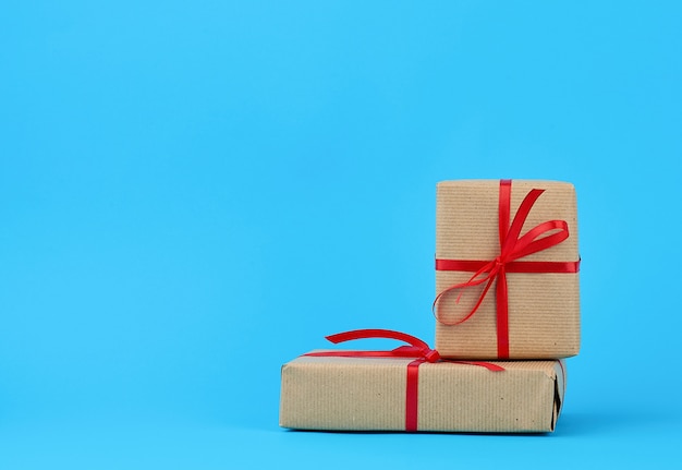 Stack of boxes wrapped in brown paper and tied with a red bow, gifts on a blue 