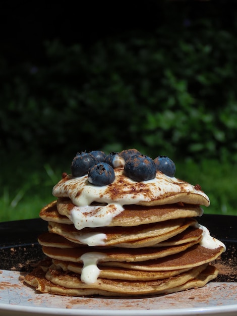 Foto una pila di pancake per la colazione al sole con lo yogurt, i mirtilli e la polvere di cacao.